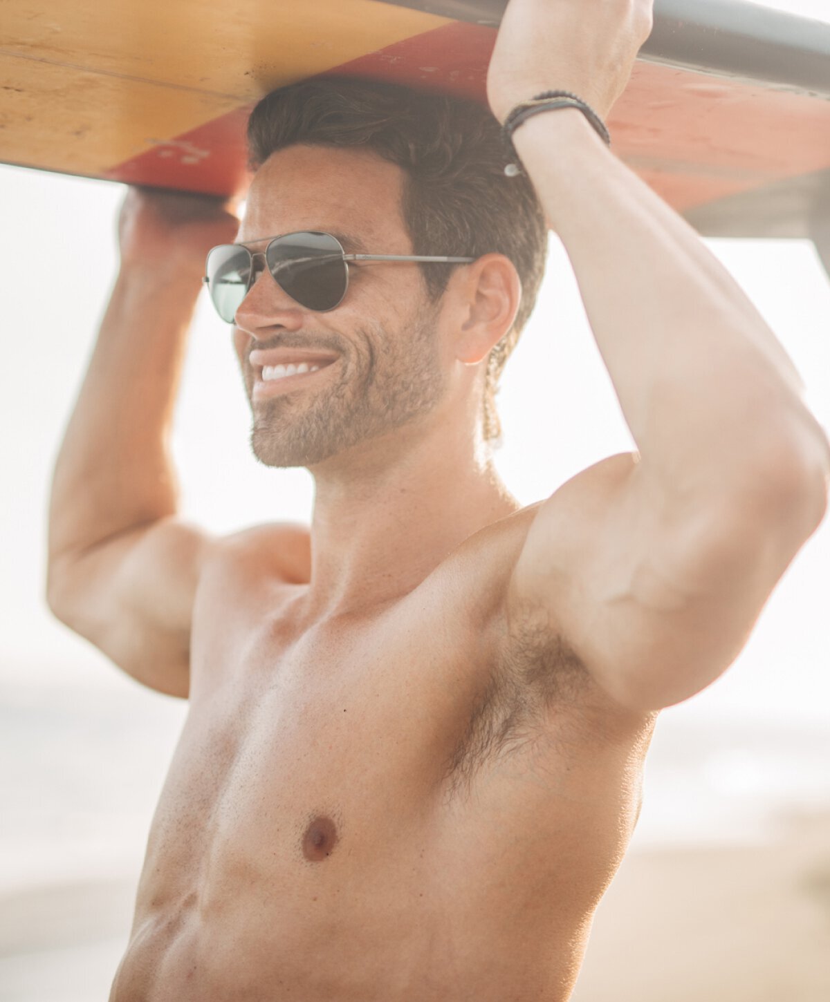 Austin gynecomastia surgery model holding a surfboard above his head
